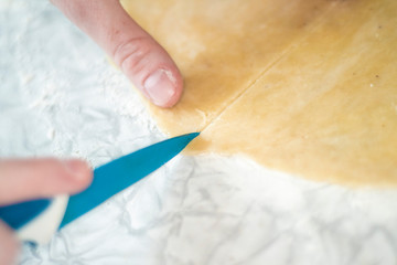 Close-up of female hands with freckles with a kitchen knife slicing dough