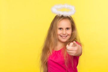 Portrait of positive happy little girl with long fair hair and angelic halo pointing finger, making...