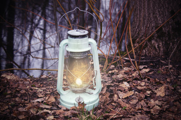 Kerosene lamp with a flame standing on dry fallen leaves against the background of a tree and a...