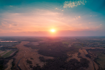 Fototapeta na wymiar Spring rural landscape in the evening with beautiful burning sky. Aerial view. Panoramic view of pine forest, fields, river, and village during blazing sunset