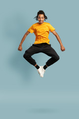 Fototapeta na wymiar Full length shot of overjoyed black man in orange t-shirt jumping and looking up