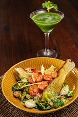 Caesar salad with prawns and parmesan cheese, croutons, tomatoes on wooden background and green cocktail