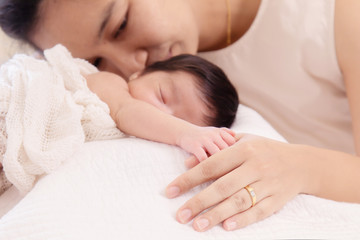 Selective focus beautiful Asian mother with wedding ring nurturing adorable infant with love and care, mom hold tiny finger newborn baby while sleeping comfortable on bed at home. motherhood lifestyle