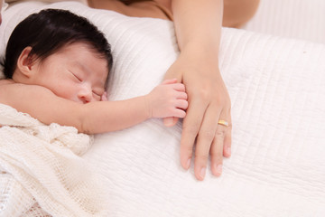Fototapeta na wymiar Selective focus touching feeling, tiny fingers newborn baby hold mother hands with wedding gold ring, mom feeding newborn at home, happy infant sleep on bed hold mother finger for protection, safety