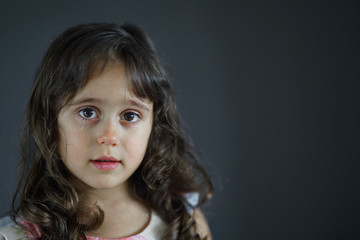 a 5 year old girl with a tear under her eye looks straight