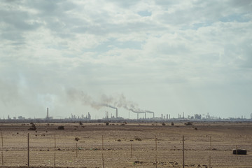 oil refinery with smokestacks fuming seen from afar in Saudi Arabia - obrazy, fototapety, plakaty