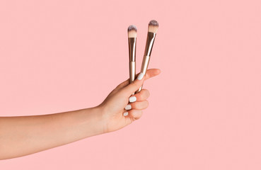 Professional makeup artist holding cosmetic brushes on pinkbackground, closeup