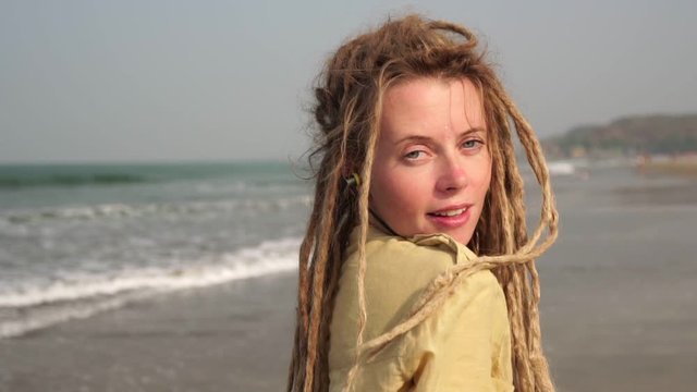A young hippie woman with dreadlocks is walking along a sandy beach in Goa