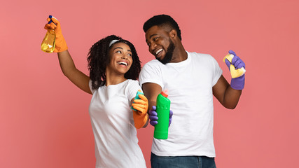 Joyful african couple with household supplies in hands over pink background