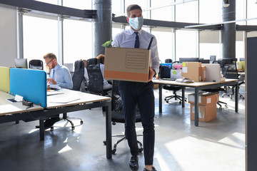 Dismissal employee in preventive medical mask in an epidemic coronavirus. Sad dismissed worker are taking his office supplies with him from office.