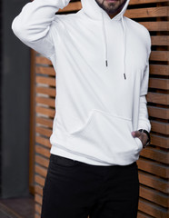 young man in white hoodie standing outdoors on wooden background