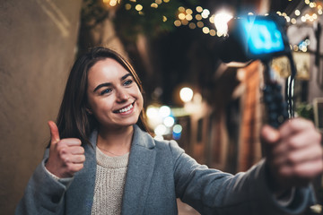 Traveler female blogger shooting video for vlog social media with digital camera showing ok or like. Smile happy woman vlogger taking photo selfie on background light night city illuminations