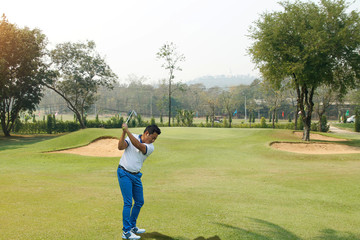 Golf player hitting shot with club on course at beautiful morning with sun flare in background