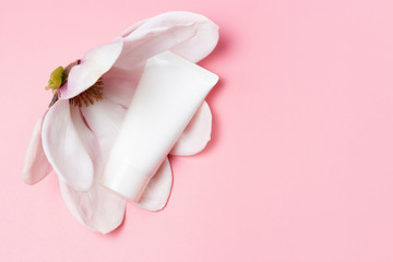 White tube with cream and magnolia flower on pink background, copy space
