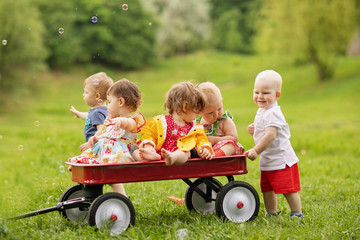 group of five toddlers riding in a red pull wagon on the farm