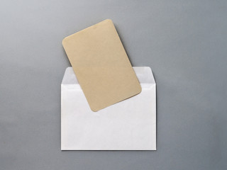 An empty Kraft brown card for an invitation or greeting and a white paper envelope on a gray textured background. Mock-up. Stylized stock photos. The view from the top.