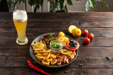 glass of foamy beer and a plate with snacks on a wooden background