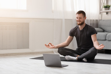 Millennial guy meditating with trainer online via laptop
