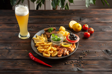 glass of foamy beer and a plate with snacks on a wooden background