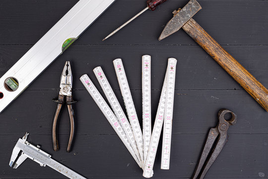 Old used hand tools on the black wooden background table board. Old wooden Hammer libella measuring meter combination pliers nonius and screwdriver