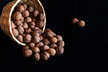 Small wicker basket filled with walnuts on a black background