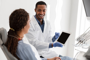 Naklejka na ściany i meble Handsome dentist showing patient empty digital tablet screen