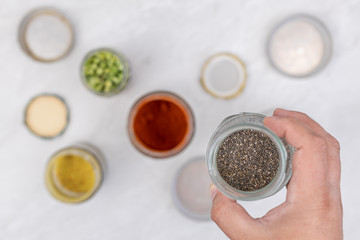 Chia seeds in the jar with jars in the blurred background on the kitchen table. Healthy food concept with chia seeds in the hand