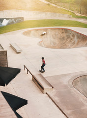 The teenage extreme boys in protection riding a skateboard and practicing the tricks at the skatepark. Urban skateboarding. Side view.