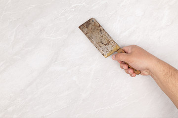 Old rusty meat chopper knife in the male hand above grey marble kitchen table top. Copy space above...