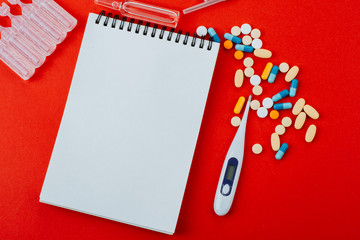 Notepad ,a medicines, a thermometer and ampoules on a red background.