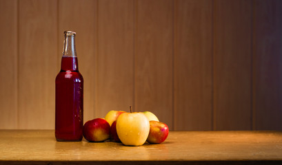 Glass bottle with red apple cider and apples on a wooden background with copy space.