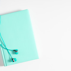White office desk. Turquoise notebook, headphones on white background. Flat lay, top view, copy space