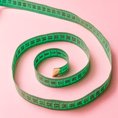 Green spiral tailor measuring tape on pink background