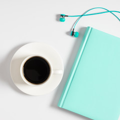 White office desk. Turquoise notebook, headphones and coffee cup on white background. Flat lay, top...