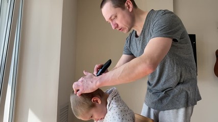 Self-isolation concept. Father cutting the hair of a little son with a hair clipper at home during the coronavirus quarantine. Self-isolation concept