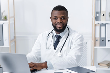 Fototapeta premium Portrait of cheerful black doctor at his workplace