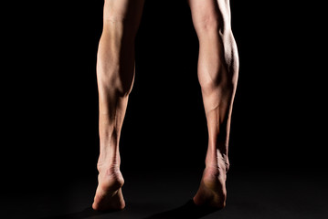 Studio photography of the legs and the calf muscle of a muscular cyclist athlete with black background