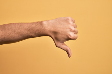 Hand of caucasian young man showing fingers over isolated yellow background doing thumbs down...