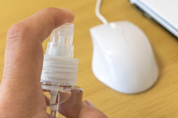 パソコンのマウスを除菌スプレーで消毒する男性
