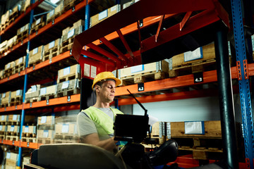 Forklift operator going through paperwork while working in a warehouse.