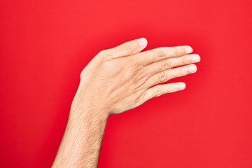 Hand of caucasian young man showing fingers over isolated red background stretching and reaching with open hand for handshake, showing back of the hand