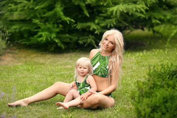 Beauty family look. Beautiful mother with daughter relax on green grass at park.  Glamour blonde...