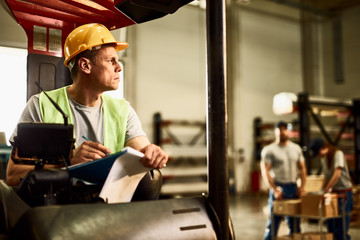 Pensive forklift driver taking notes in industrial warehouse. © Drazen