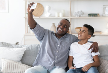 Home Selfie. Smiling black grandfather with preteen grandson taking photo together
