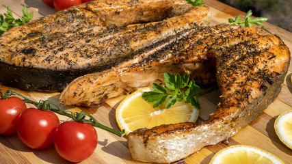 Baked salmon fish steak with tomatoes, herbs, lemon slice and spices. Smoked trout on green grass. Grilled seafood with vegetables on wooden table. Diet menu