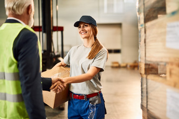 Happy female warehouse worker handshaking with senior businessman.