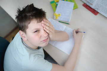 A teenager boy sits at a table in his room, doing homework. He's bored. Portrte, close-up, top view