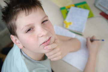 Naklejka premium A teenager boy in his room sits at a table and does homework. Thinking. Portrait, close-up. View from above