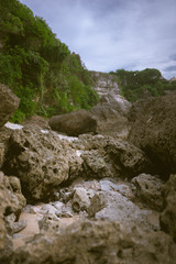 Beautiful deserted beach on the island of Bali at sunset. Rocks and nature. Plants and houses on the coast. Tropical paradise. Stones and white sand on the ocean