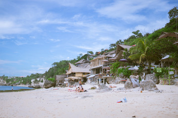 Beautiful deserted beach on the island of Bali at sunset. Rocks and nature. Plants and houses on the coast. Tropical paradise. Stones and white sand on the ocean